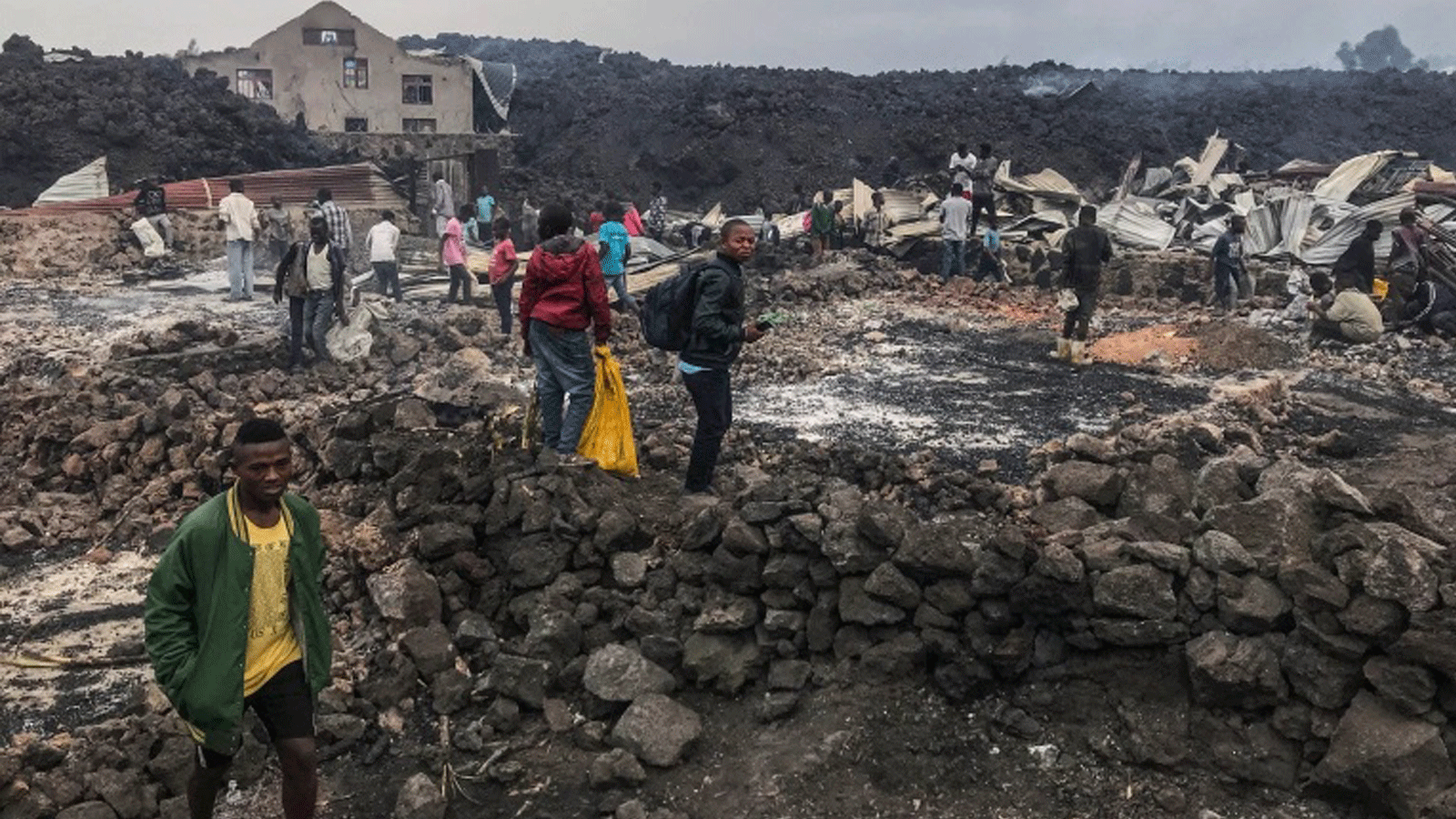 سكان يقفون بجوار مبانٍ مدمرة وبالقرب من الرماد المحترق في الصباح الباكر في غوما شرق جمهورية الكونغو الديمقراطية