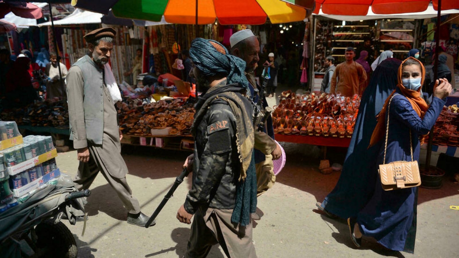 امرأة تنظر إلى الوراء بينما كان مقاتل من طالبان (وسط) يسير بجوار المتسوقين على طول سوق منداوي في كابول. بتاريخ 1 أيلول/ سبتمبر 2021.