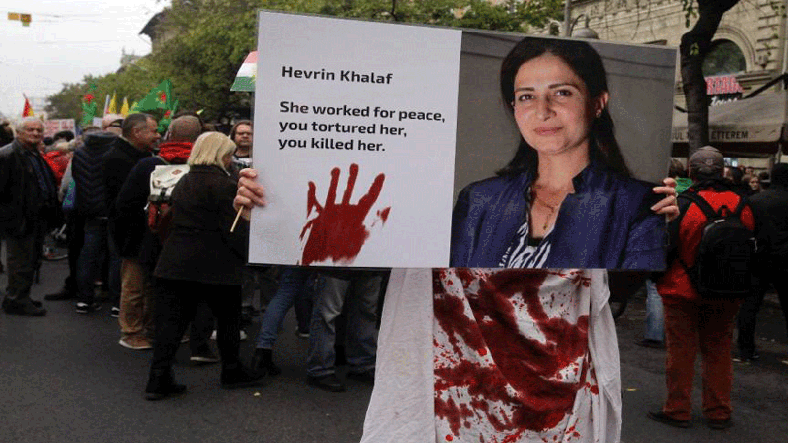 متظاهرون يحملون ملصقًا عليه صورة السياسية الكردية هفرين خلف التي أعدمها أفراد من الجيش الوطني السوري، خلال مظاهرة في 7 نوفمبر 2019، في بودابست، المجر. 