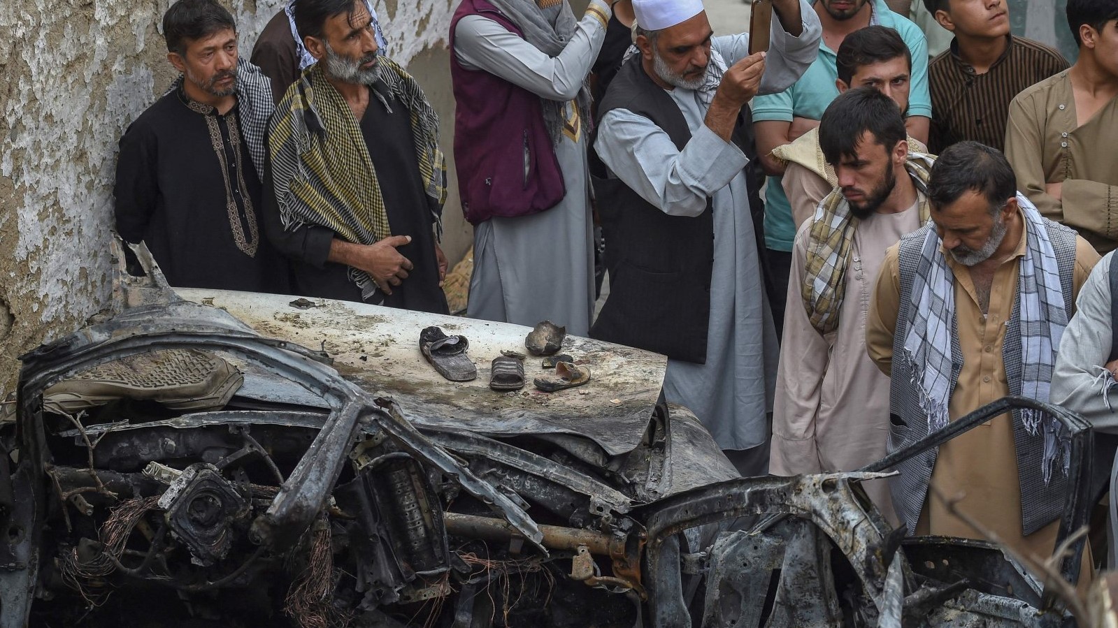 سكان أفغان وأفراد عائلات ضحايا يتجمعون بجوار سيارة مدمرة قرب منزل في اليوم التالي لغارة جوية أميركية بطائرة مسيرة في كابول، أفغانستان، في 30 أغسطس 2021
