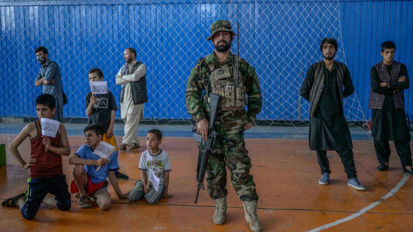 مقاتل من طالبان يقف بينما ينتظر شباب لإظهار مهاراتهم في صالة ألعاب رياضية في كابول، حدث تم تنظيمه لزيارة رئيس الرياضة الأفغاني الجديد بشير أحمد رستمزاي.