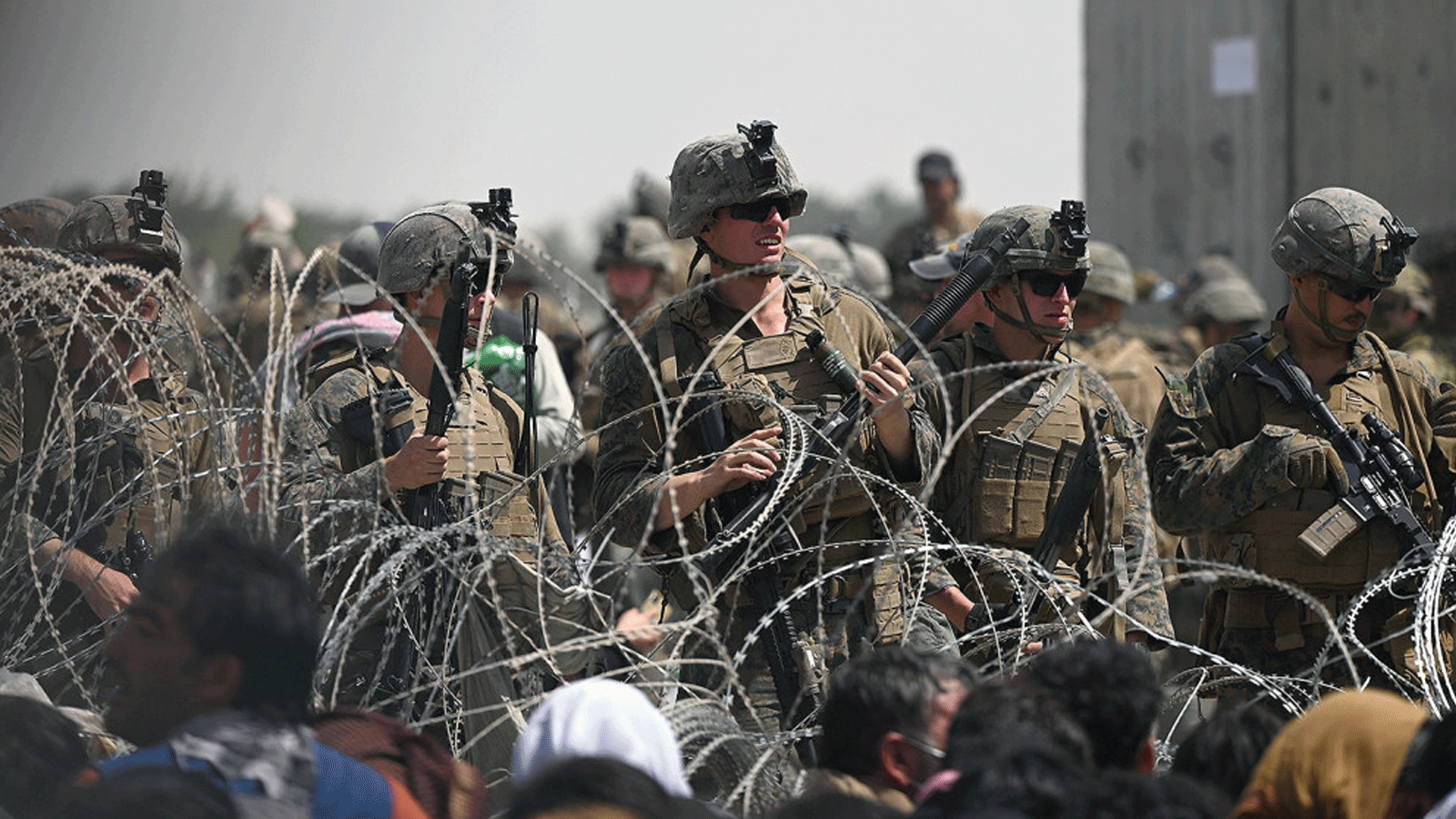 جنود أمريكيون يقفون وراء الأسلاك الشائكة بينما يجلس الأفغان الذين يأملون في الفرار من البلاد بعد استيلاء طالبان العسكري على جانب الطريق بالقرب من المطار في كابول في 20 آب/أغسطس 2021