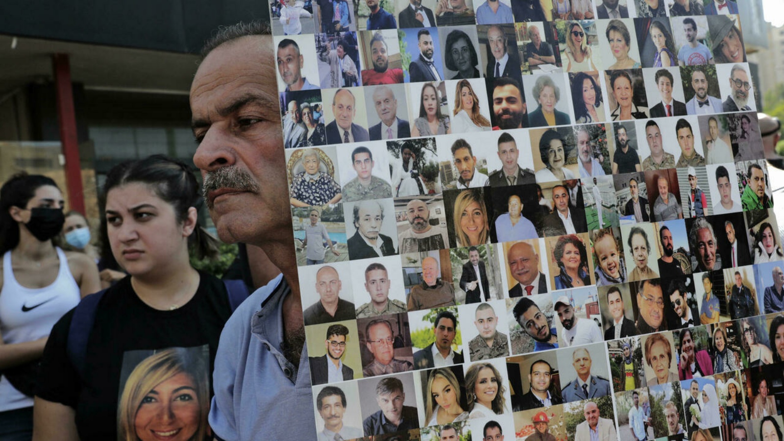 رجل يحمل لافتة تُظهر وجوه ضحايا انفجار مرفأ بيروت 2020 كمتظاهرين وأفراد عائلات الضحايا في تظاهرة أمام قصر العدل.