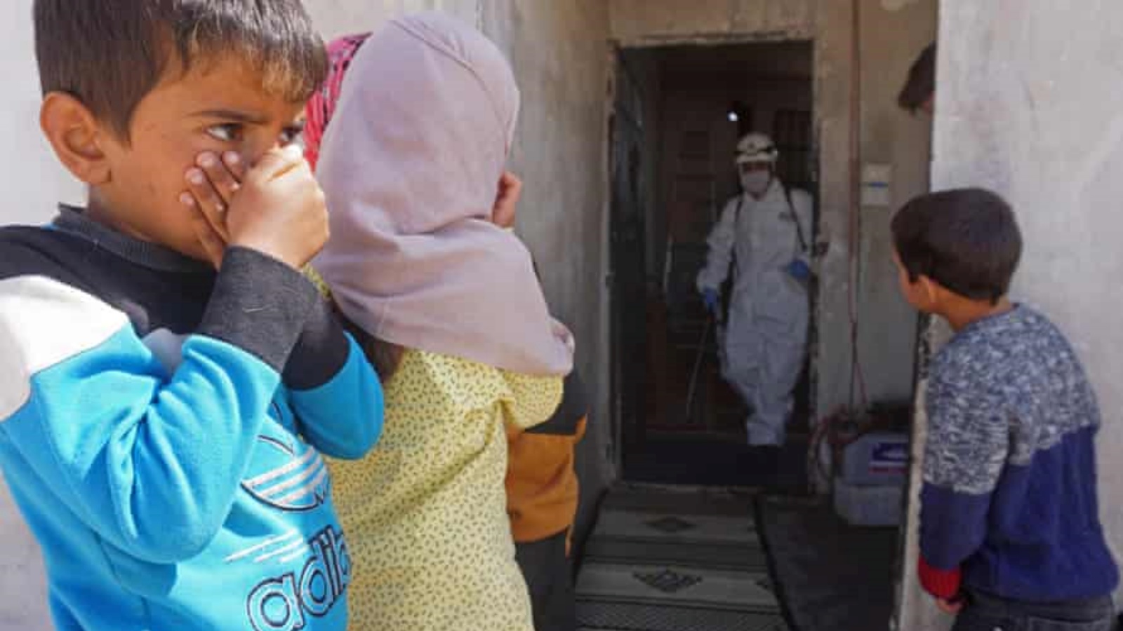 أطفال سوريون يشاهدون أحد عناصر طاقم التعقيم يطهر مبنى تسكنه عائلات نازحة في بلدة بنش الخاضعة لسيطرة المعارضة في محافظة إدلب.
