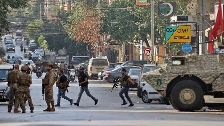 مسلحون لحركة أمل وحزب الله يمرون أمام آلية وجنود للجيش اللبناني الخميس في منظقة الاستباكات شرق بيروت