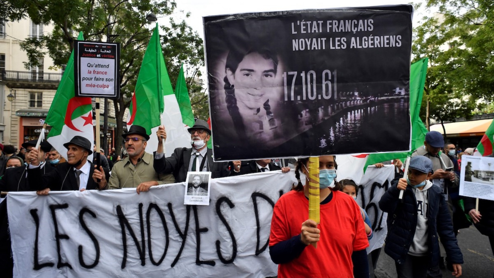 أشخاص يحملون لافتات وأعلام جزائرية خلال مسيرة لإحياء ذكرى القمع الوحشي لمظاهرة 17 تشرين الأول/أكتوبر 1961 والتي قُتل خلالها ما لا يقل عن 120 جزائريًا خلال احتجاج لدعم استقلال الجزائر، بالقرب من جسر بونت نوف في 17 تشرين الأول/أكتوبر 2021 في باريس.