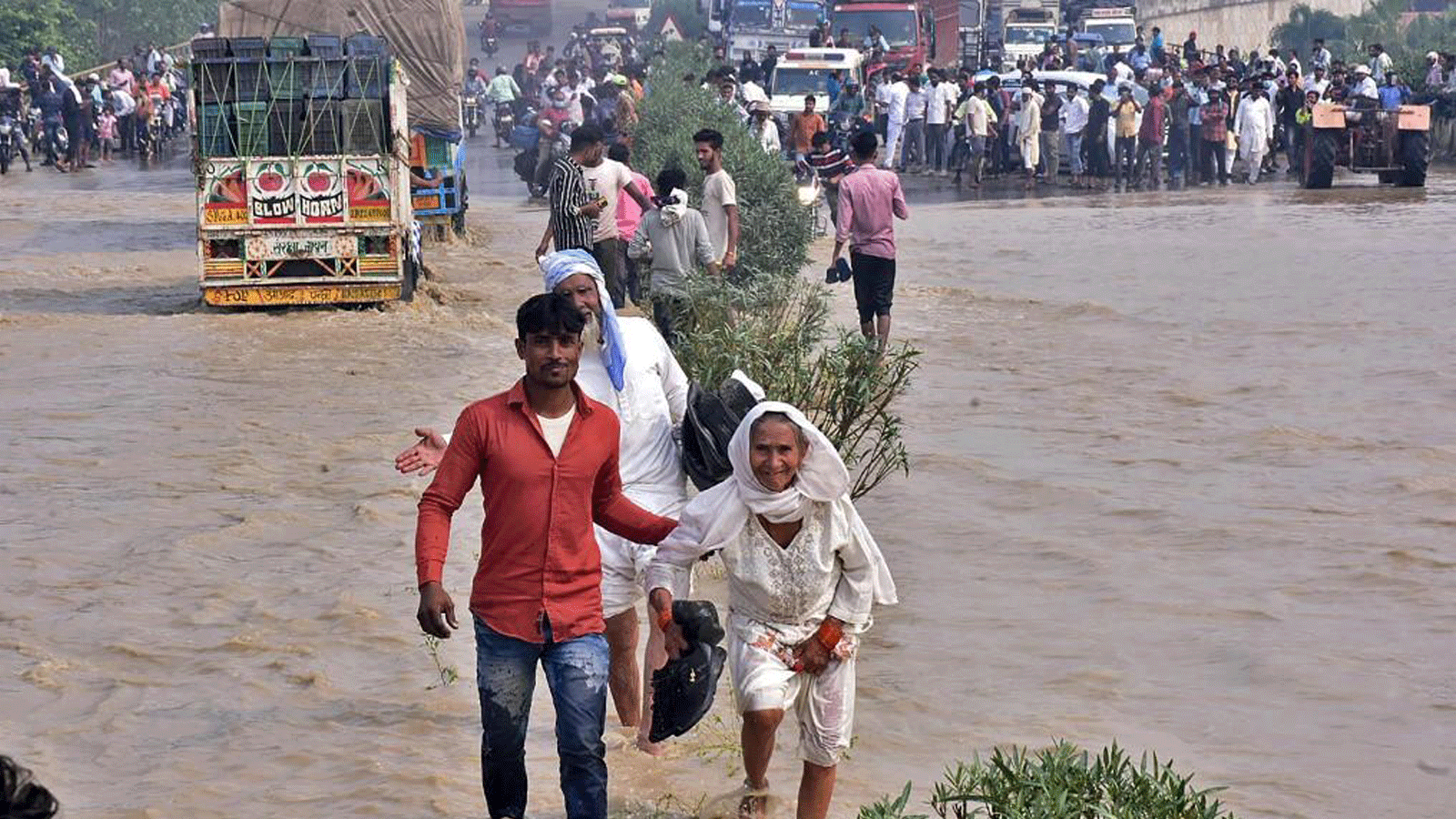 مسافرون يمرون عبر طريقٍ سريع وطني غمرته الفيضانات بعد أن فاض نهر كوسي جراء هطول أمطار غزيرة بالقرب من رامبور في ولاية أوتار براديش الهندية في 20 أكتوبر 2021 ، حيث تجاوز عدد القتلى من أيام الفيضانات والانهيارات الأرضية في الهند ونيبال 100 شخص.