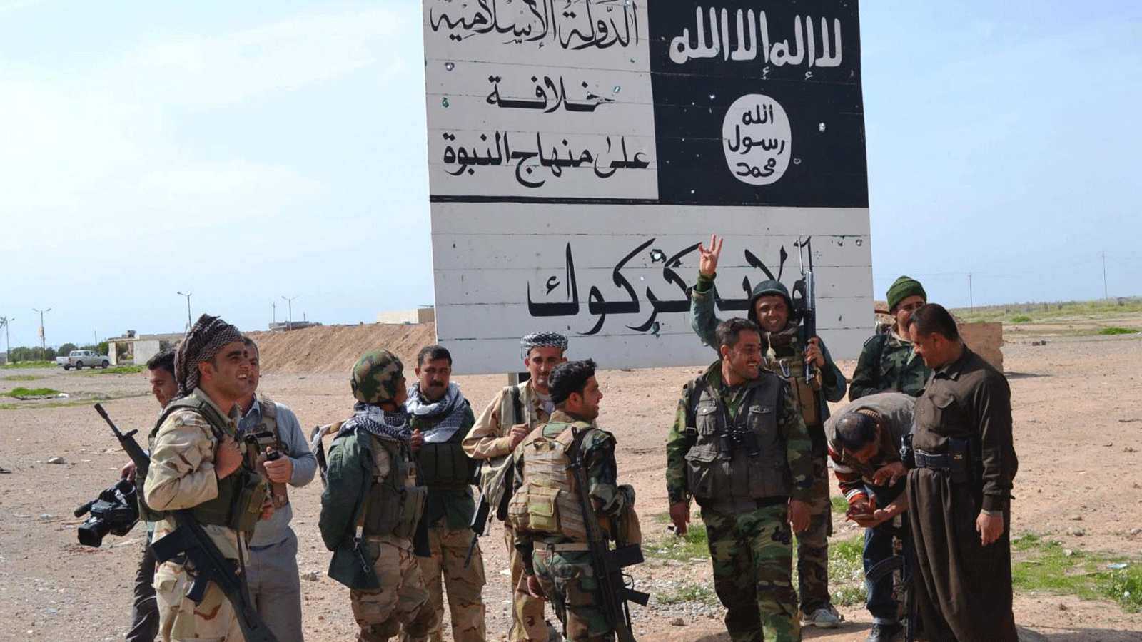 قوات كردية أمام لافتة لتنظيم الدولة الإسلامية خلال معركة الحويجة