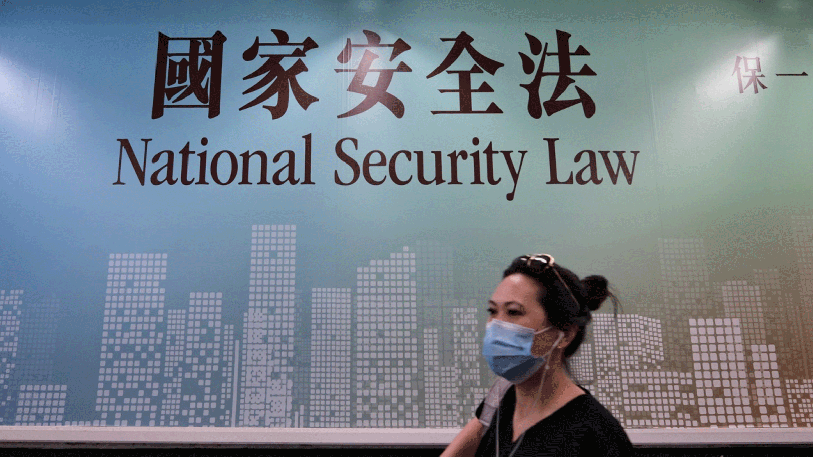 صورة لسيدة تسير جنب لافتة إشعار عامة حكومية لقانون الأمن القومي في هونغ كونغ.