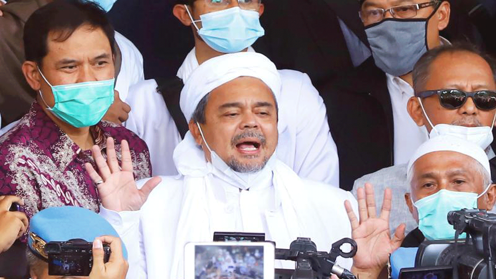 رجل الدين المسلم الإندونيسي رزيق شهاب، وسط الصورة، يحيط به أنصاره لدى وصوله إلى مقر الشرطة في جاكرتا يوم السبت، قبل اعتقاله.