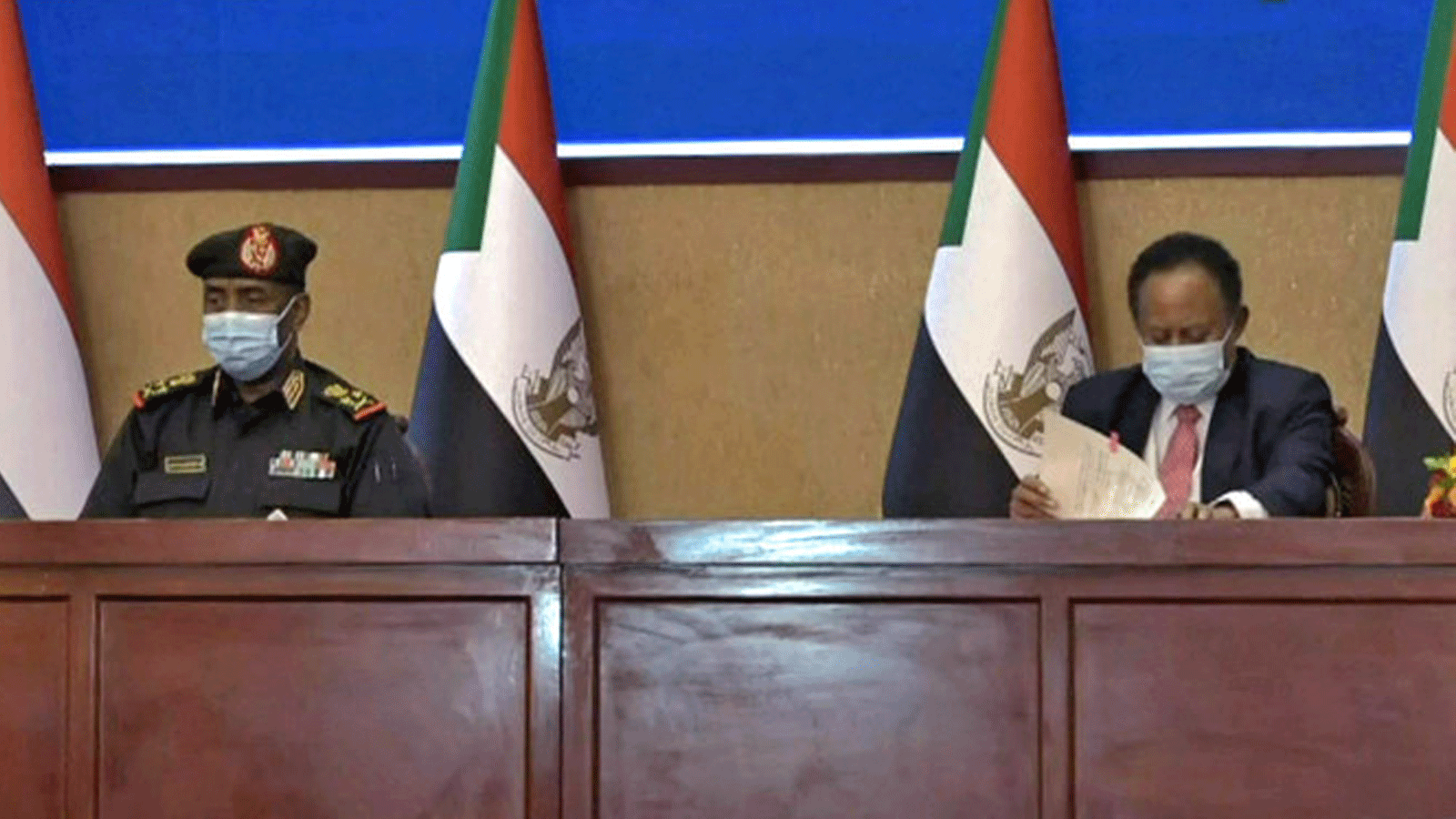  اللواء السوداني عبد الفتاح البرهان (إلى اليسار) ورئيس الوزراء عبد الله حمدوك يوقعان اتفاقًا لإعادة الانتقال إلى الحكم المدني في البلاد في 21 تشرين الثاني/نوفمبر 2021