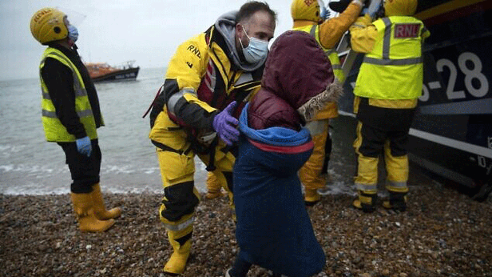 تمت مساعدة المهاجرين على الشاطئ من قارب نجاة RNLI (المؤسسة الملكية الوطنية لقوارب النجاة) على شاطئ في Dungeness، على الساحل الجنوبي الشرقي لإنجلترا. في 24 تشرين الثاني/ نوفمبر 2021، بعد إنقاذهم أثناء عبورهم القناة الإنجليزية. 