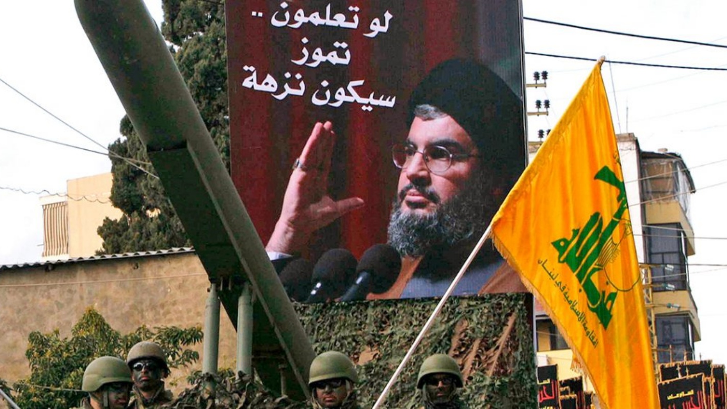 مقاتلون يقفون بجانب صاروخ لحزب الله يظهر على خلفية ملصق لزعيم الحزب حسن نصر الله. (أرشيفية)