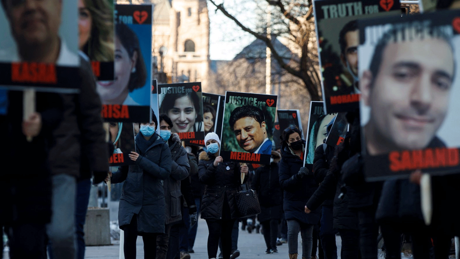  أشخاص يحملون لافتات عليها صور ضحايا طائرة الخطوط الجوية الدولية الأوكرانية المسقطة PS752، والتي أسقطها الحرس الثوري الإيراني بالقرب من طهران، بينما تتجمع العائلة والأصدقاء للمشاركة في مسيرة للاحتفال بالذكرى السنوية الأولى، في تورنتو، أونتاريو، كندا في 8 كانون الثاني/يناير 2021