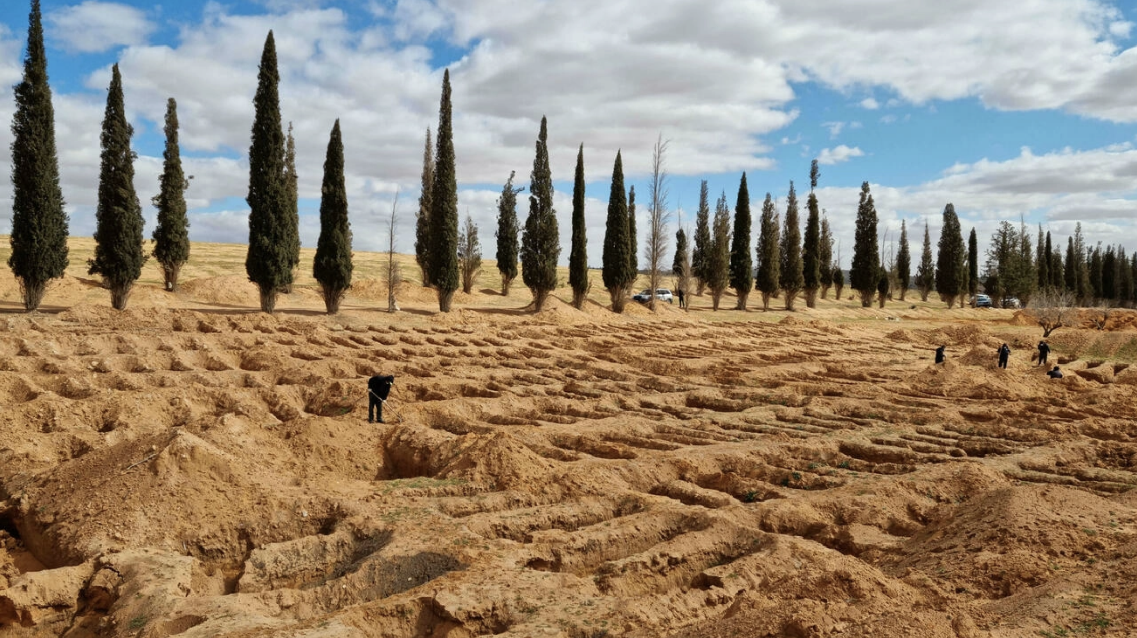 ليبيون يسيرون حول مقابر جماعية انتشلت منها جثث في مدينة ترهونة في غرب ليبيا، في التاسع من شباط/فبراير 2022