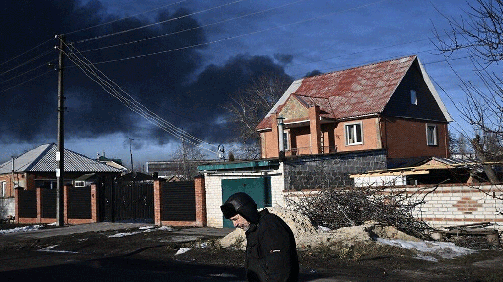 رجل يسير في شارع بينما يتصاعد دخان أسود من مطار عسكري في تشوجوييف بالقرب من خاركيف في 24 شباط\ فبراير 2022 