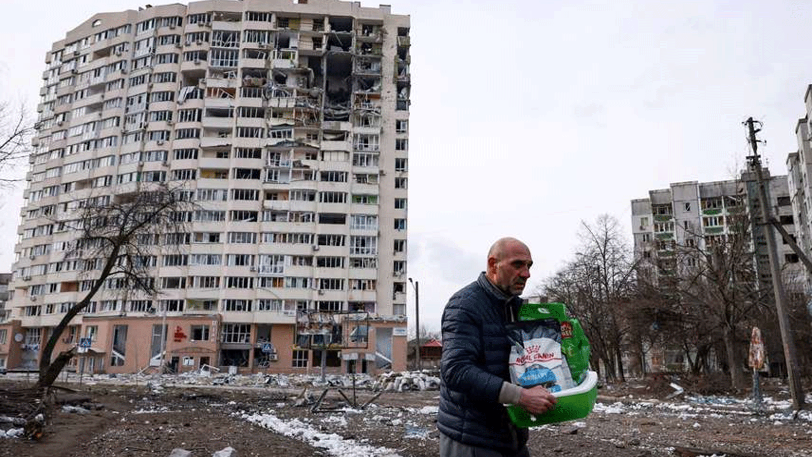 رجل يحمل أغراضه في المدينة وتبدو مخلفات القصف على المباني