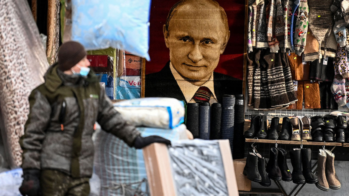 بائع يقف أمام صورة الرئيس الروسي فلاديمير بوتين في أحد الأسواق في موسكو