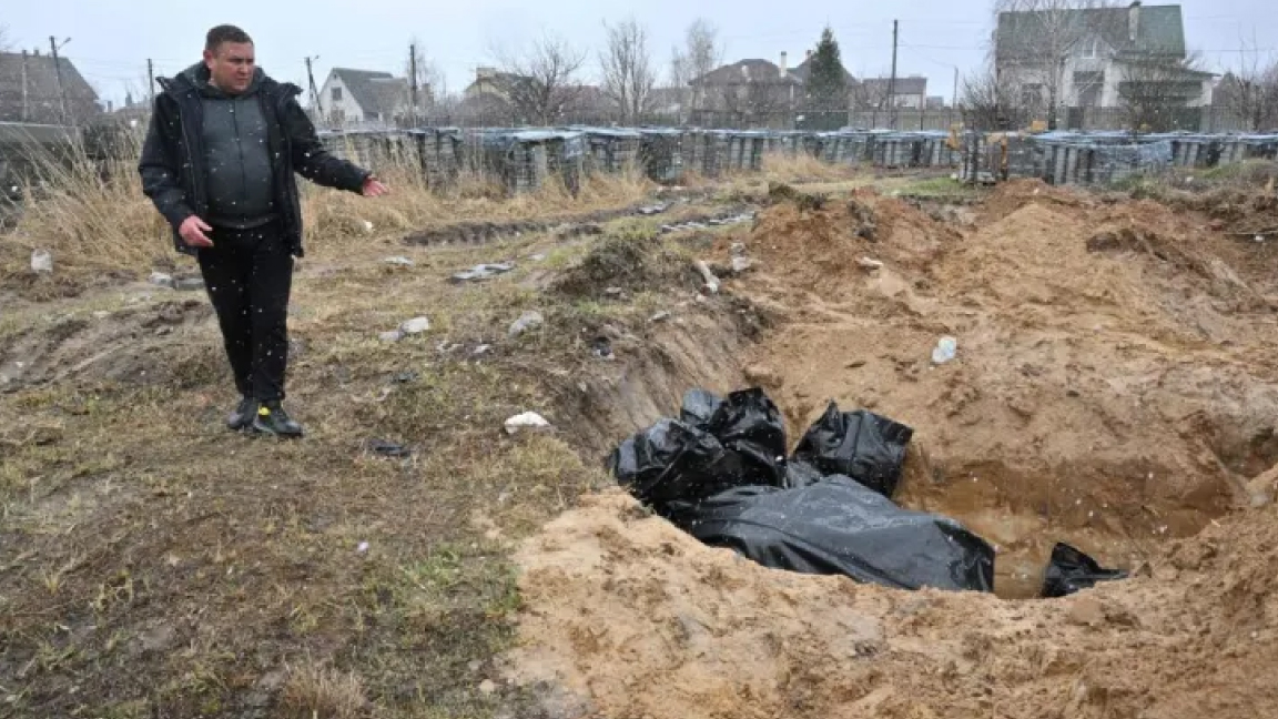 رجل يشير إلى مقبرة جماعية في بلدة بوتشا ، شمال غرب العاصمة الأوكرانية كييف في 3 أبريل 2022