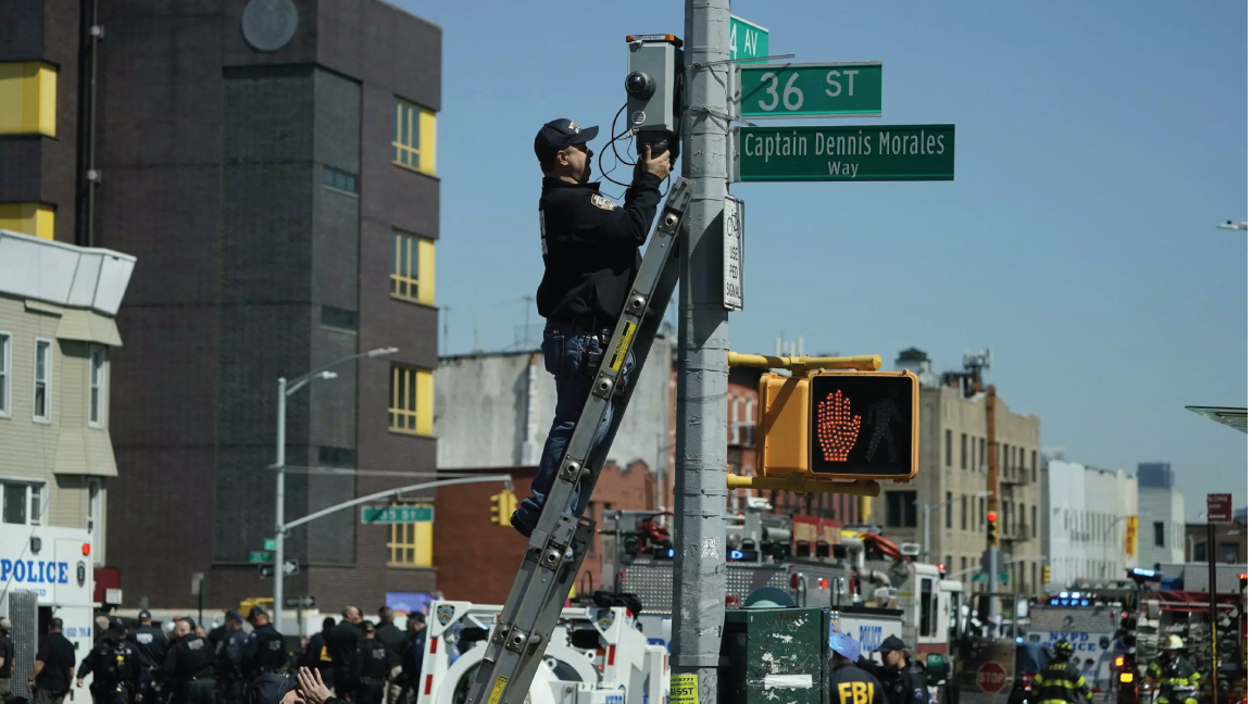 أحد أفراد إدارة شرطة نيويورك يتسلق سلمًا لاستعادة كاميرا أمنية بالقرب من محطة مترو أنفاق في مدينة نيويورك في 12 أبريل 2022 ، بعد إصابة ما لا يقل عن 16 شخصًا خلال إطلاق نار في ساعة الذروة