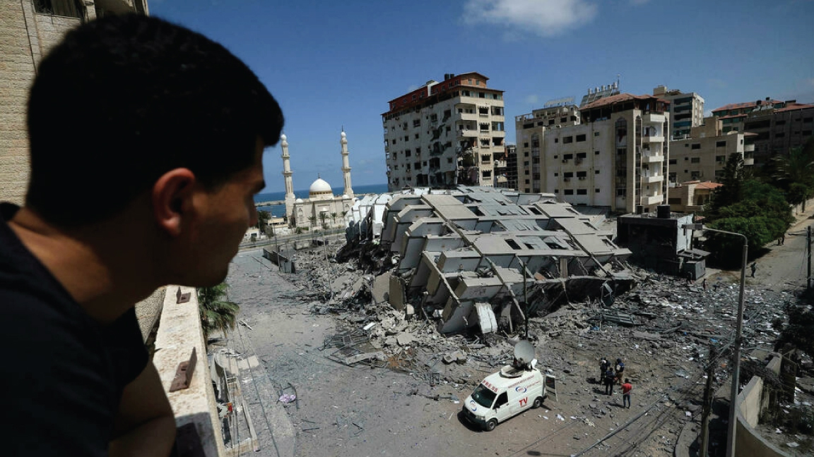 فلسطيني ينظر إلى مبنى مدمر في مدينة غزة، بعد سلسلة من الغارات الجوية الإسرائيلية على قطاع غزة الذي تسيطر عليه حماس في وقت مبكر من 12 مايو 2021