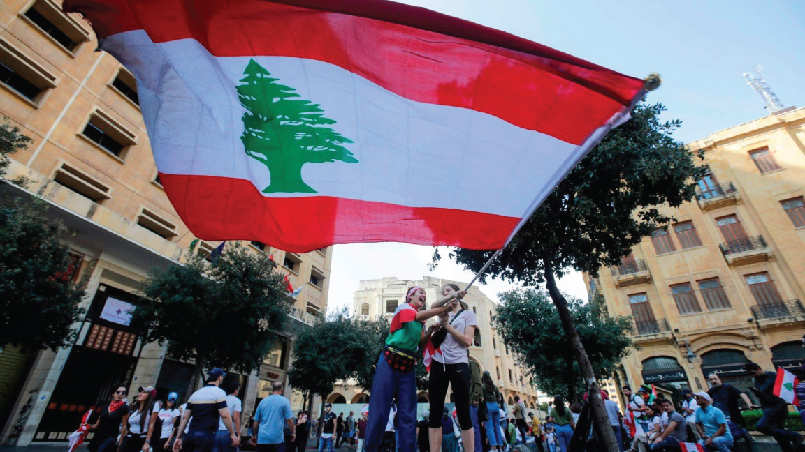 شبان وشابات في أوائل أيام الاحتجاج بعد 17 أكتوبر 2019 في وسط بيروت يرفعون العلم اللبناني ويرفضون هيمنة سلاح حزب الله على الدولة اللبنانية
