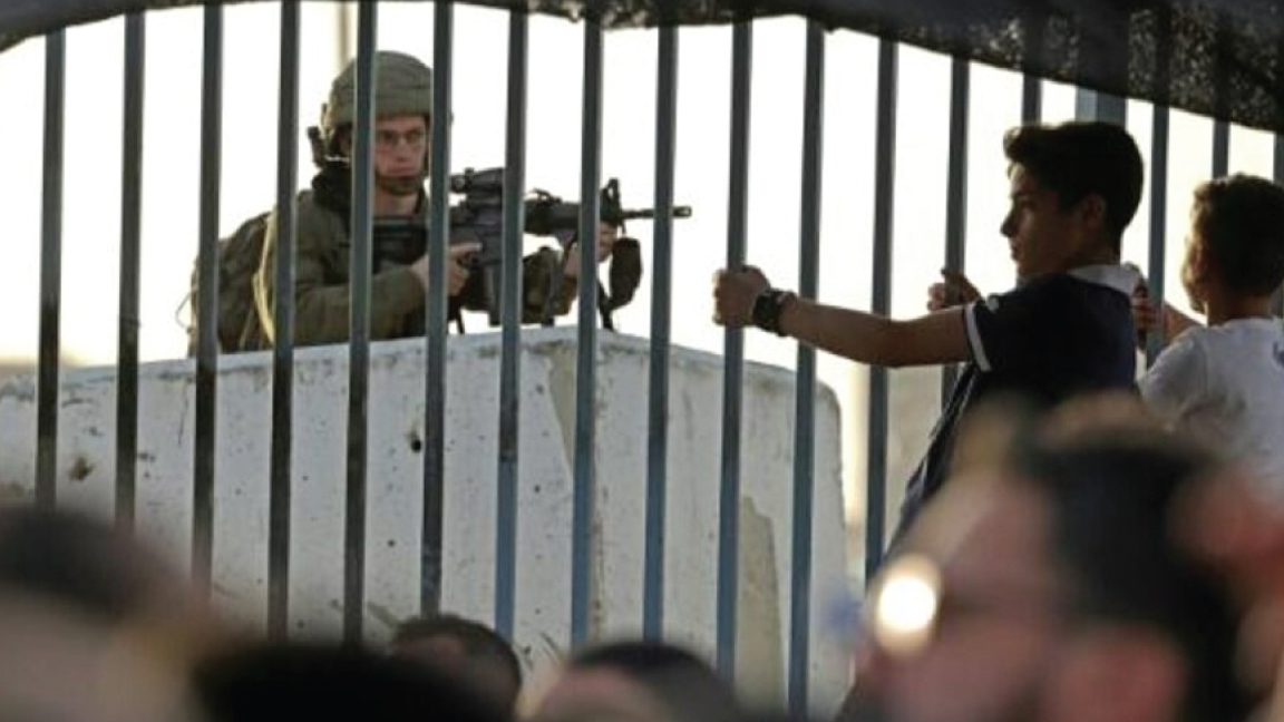جندي إسرائيلي متأهب بسلاحه أثناء وصول فلسطينيين بأعداد كبيرة إلى حاجز قلنديا في الصفة الغربية المحتلة للعبور إلى المسجد الأقصى في القدس في27 ديسمبر 2021