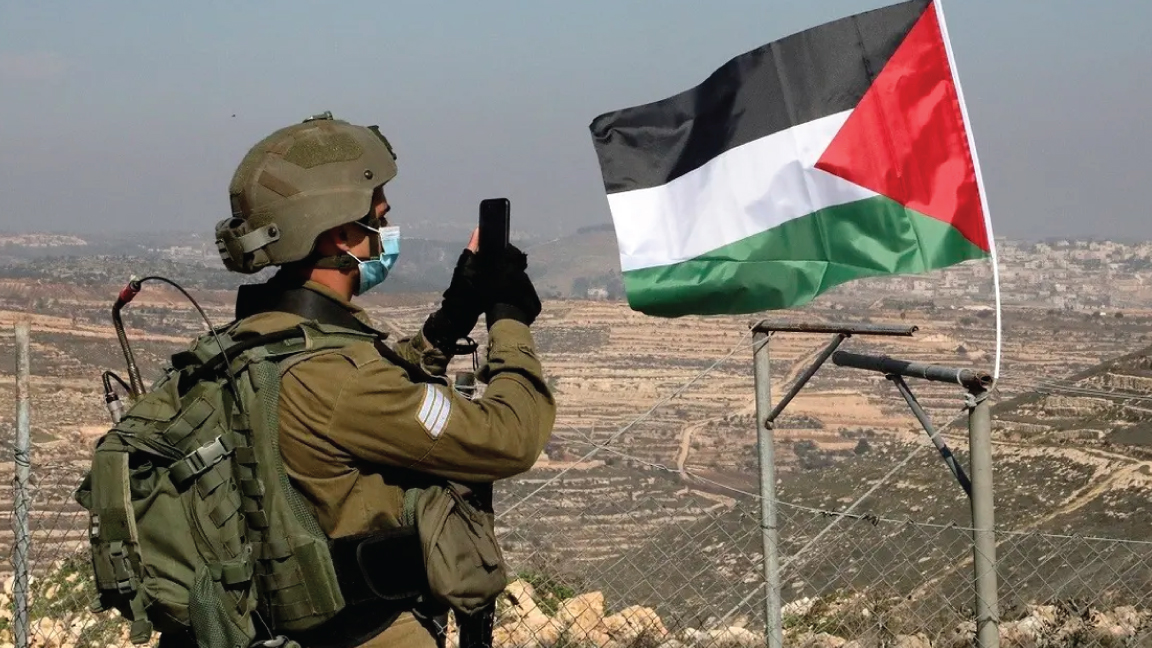 عنصر في قوات الأمن الإسرائيلية يلتقط صوراً لمتظاهرين فلسطينيين يحاولون الوصول إلى أراضيهم التي صادرتها السلطات الإسرائيلية، في الضفة الغربية المحتلة، 4 يناير 2021