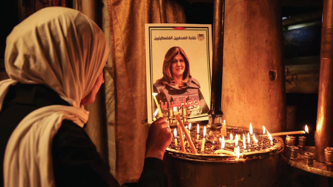 سيدة تضيء شمعة في كنيسة المهد في مدينة بيت لحم جنوب الضفة الغربية المحتلة أمام صورة للصحافية شيرين ابو عاقلة التي قتلت بالرصاص خلال تغطيتها عملية أمنية إسرائيلية في جنين (شمال) في 11 مايو 2022