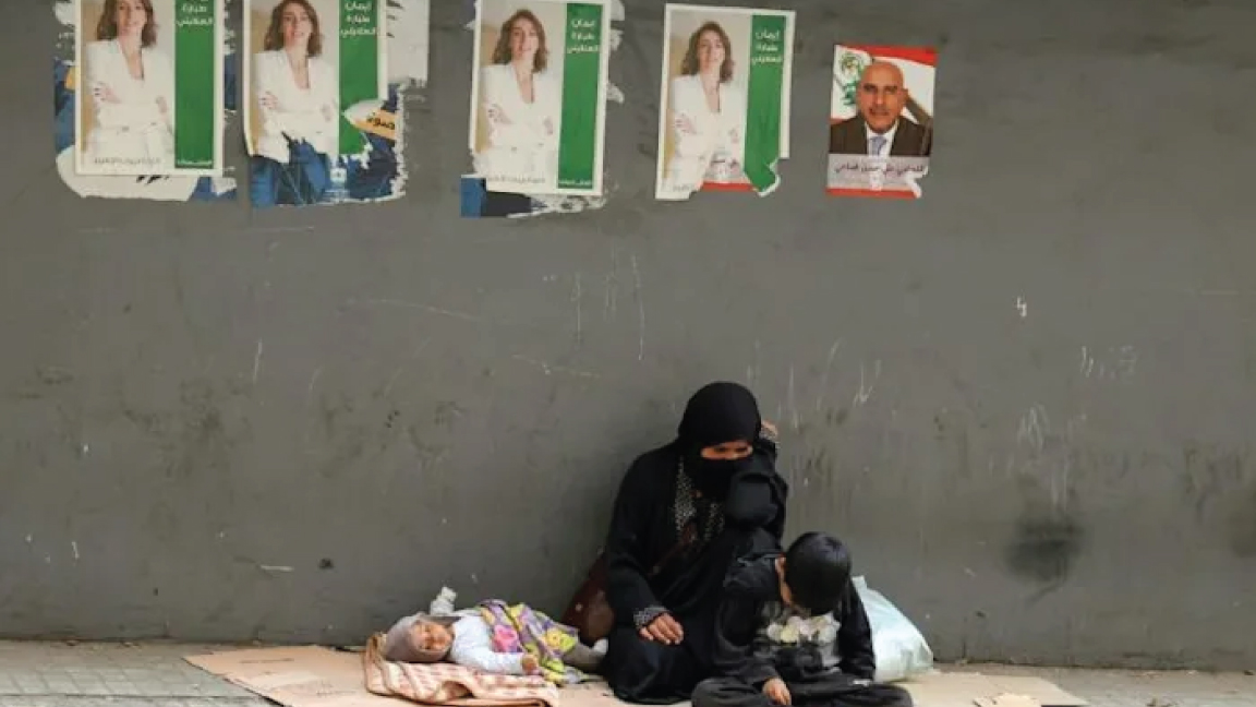 متسولة وطفلاها يجلسون تحت ملصقات انتخابية على أحد الأرصفة في بيروت