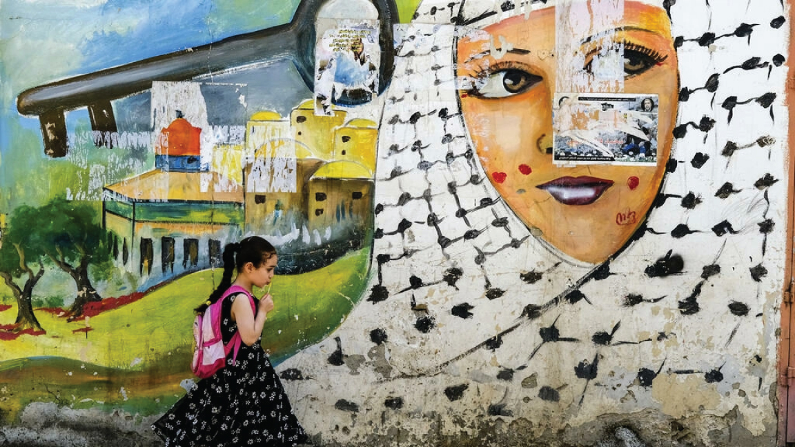 فتاة تمر قرب رسم جداري في مخم جنين للاجئين في الضفة الغربية المحتلة في 19 أيار/مايو 2022
