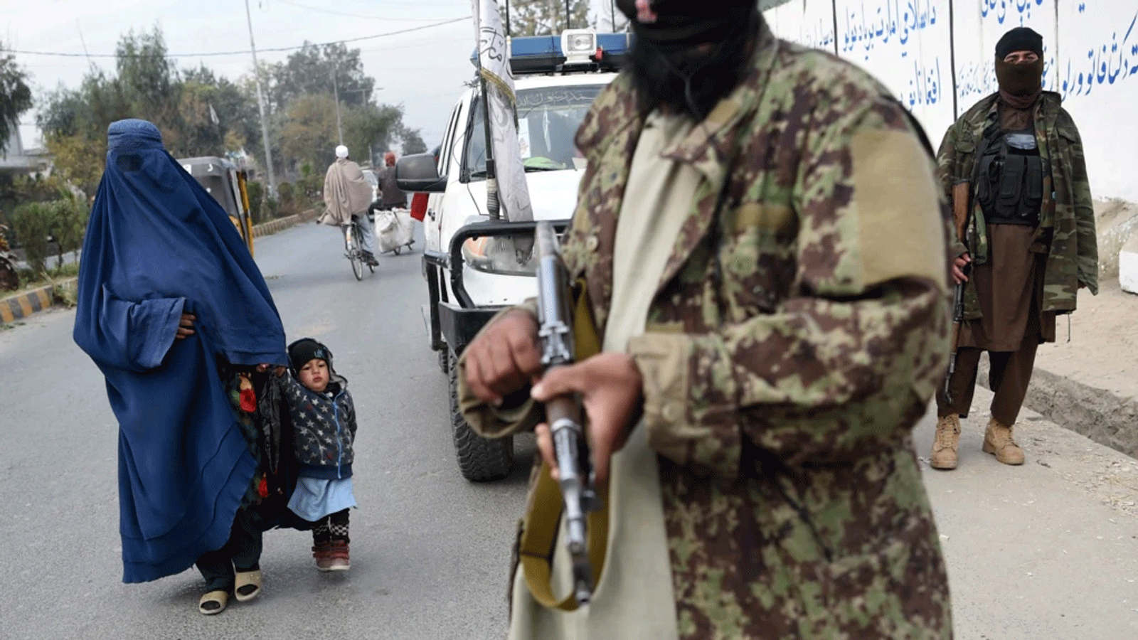 امرأة ترتدي البرقع وطفل يمشيان بجوار مقاتلي طالبان على جانب طريق في جلال آباد، أفغانستان 