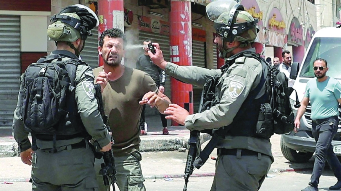 جندي من حرس الحدود الإسرائيلي يرش غاز الفلفل على وجه متظاهر فلسطيني خلال اشتباكات في بلدة حوارة بالضفة الغربية الجمعة