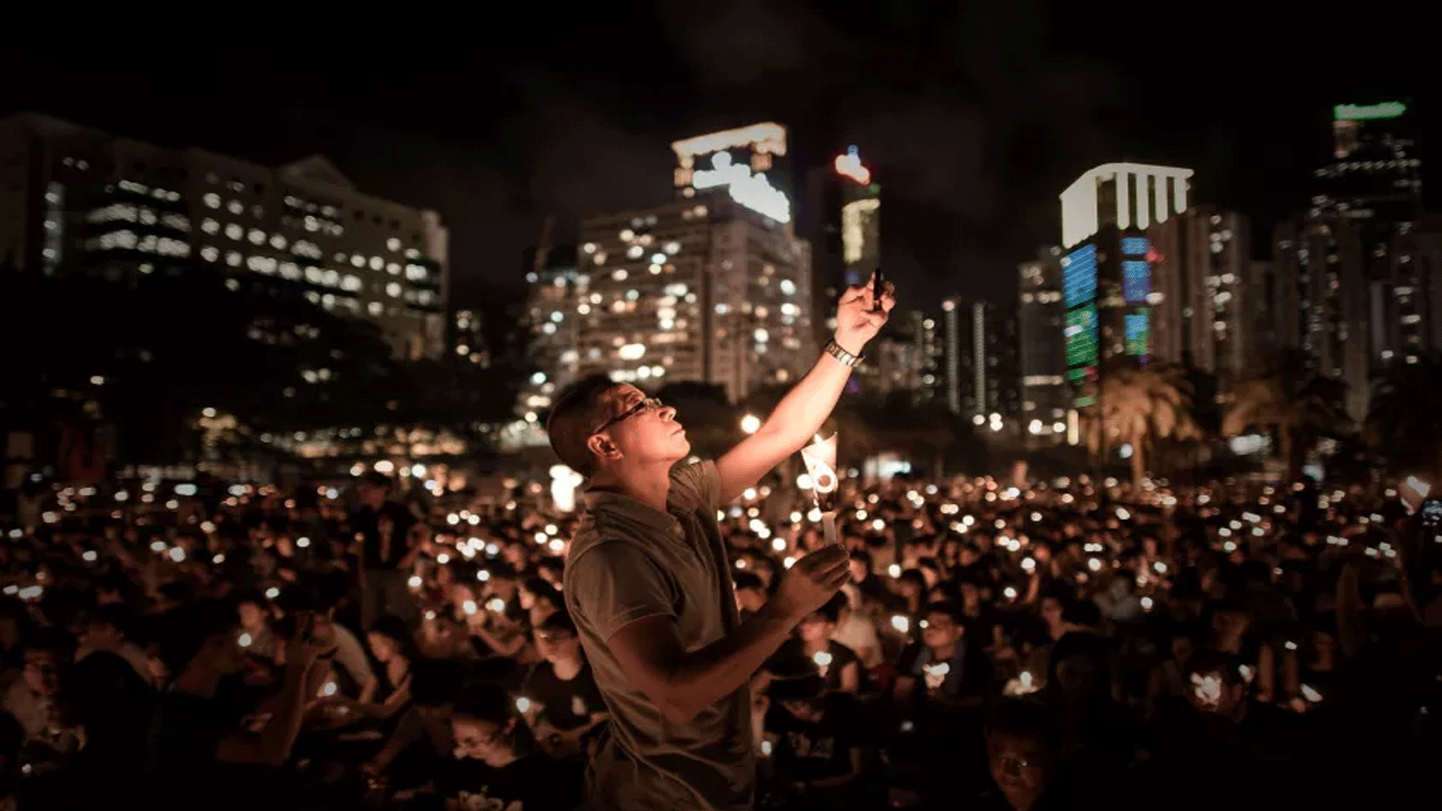 رجلٌ يلتقط صورة بهاتفه بينما يحمل آخرون الشموع في وقفة احتجاجية في هونغ كونغ لإحياء الذكرى الخامسة والعشرين لـ
