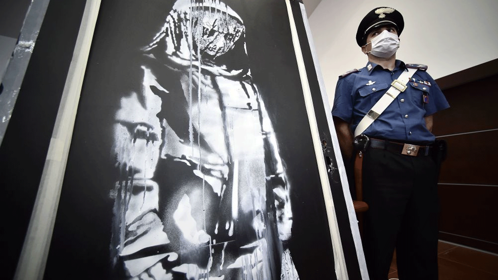 رجل شرطة يقف بالقرب من قطعة فنية منسوبة إلى بانكسي، سُرقت في باتاكلان في باريس عام 2019، وعُثر عليها في إيطاليا، قبل مؤتمر صحفي في لاكويلا في 11 حزيران\ يونيو 2020.