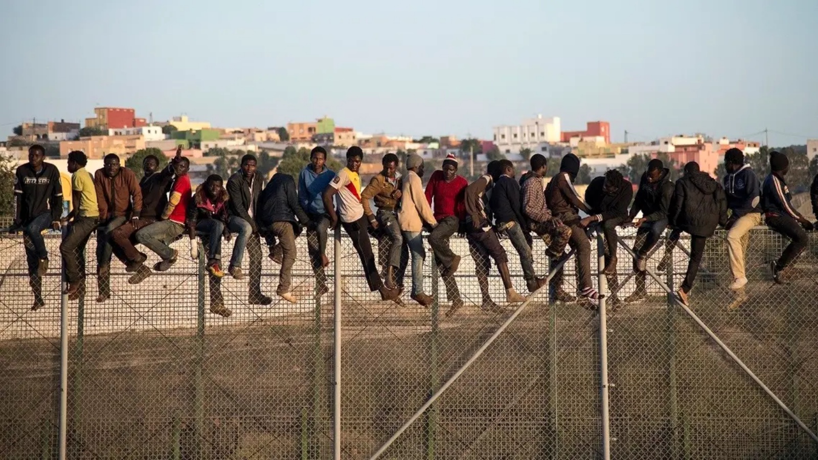 مهاجرون محتملون يقفون فوق سياج حدودي يفصل المغرب عن جيب مليلية الإسباني في شمال أفريقيا