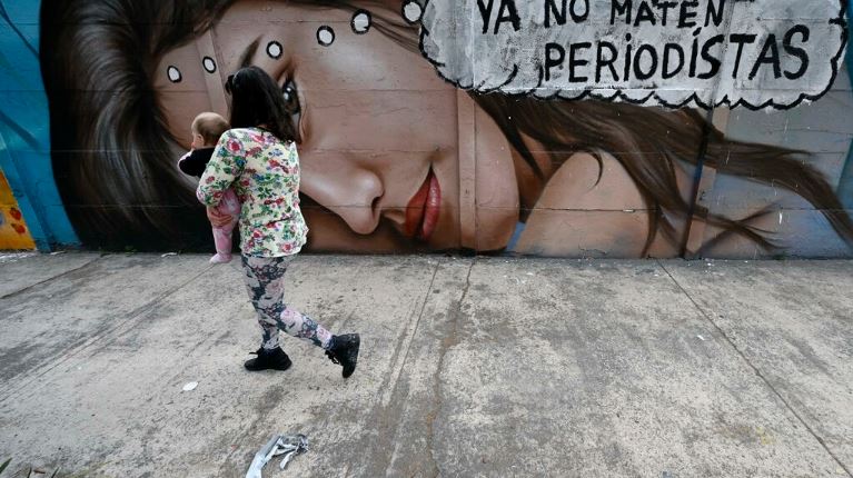 امرأة تحمل طفلاً تمشي أمام لوحة جدارية كُتب عليها 