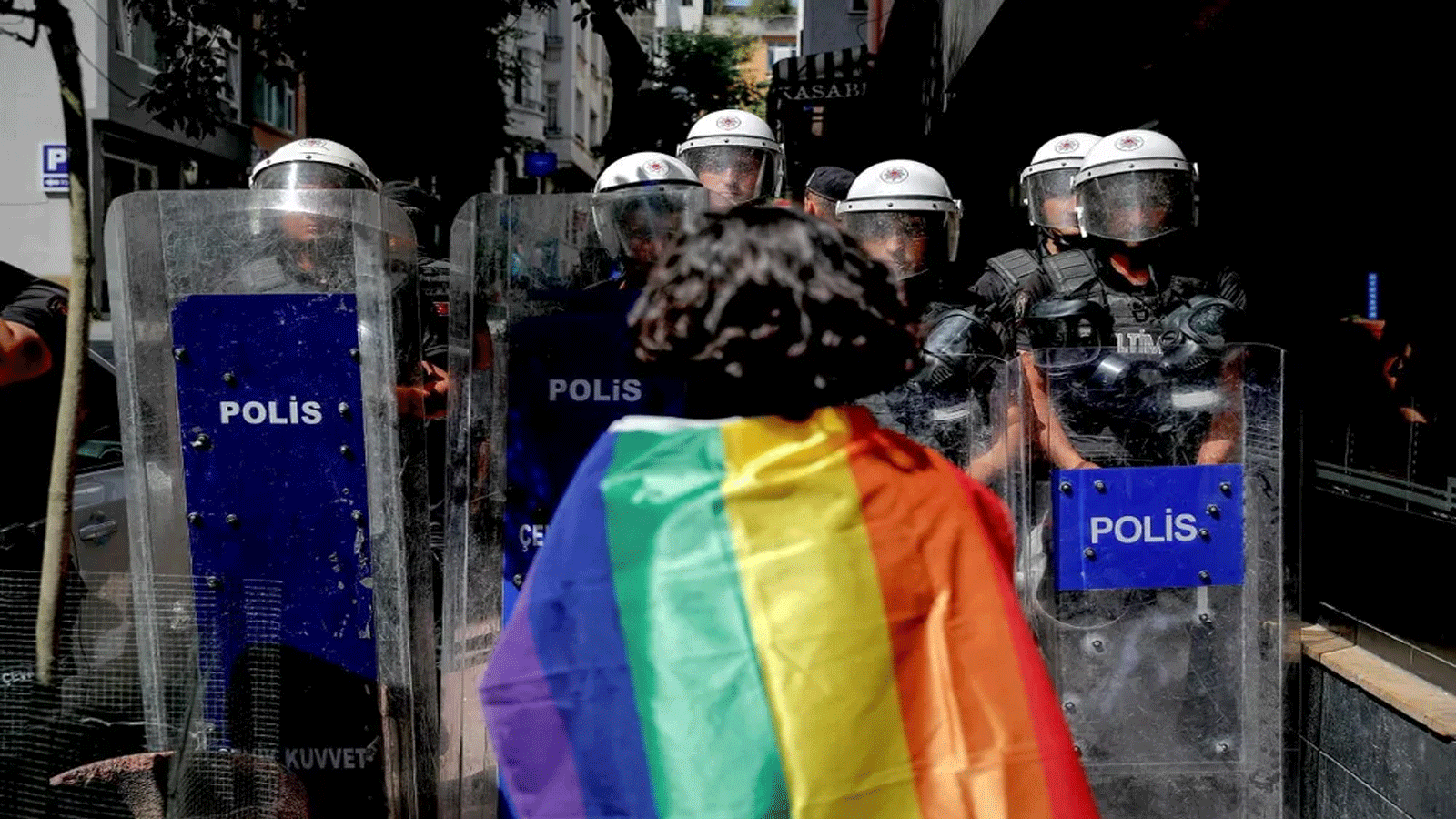 متظاهر يرتدي علم قوس قزح ويواجه رجال شرطة مكافحة الشغب خلال مسيرة فخر في اسطنبول، تركيا، في 26 حزيران\ يونيو 2022.