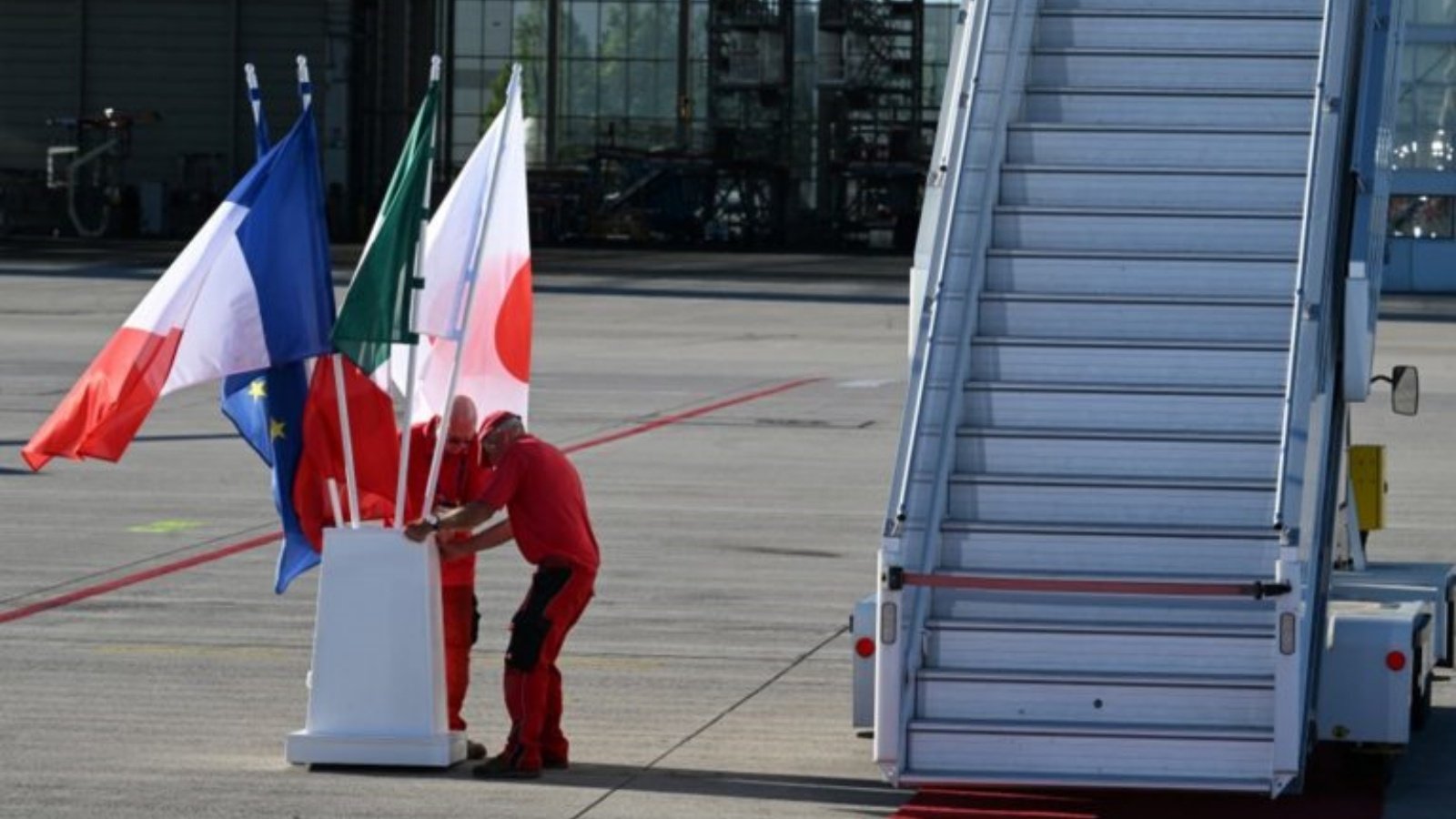 موظفو المطار يرفعون أعلام اليابان وإيطاليا وفرنسا والاتحاد الأوروبي قبل وصول قادة مجموعة السبع إلى مطار فرانز جوزيف شتراوس في ميونيخ، جنوب ألمانيا، في 25 يونيو 2022، عشية قمة مجموعة السبع.