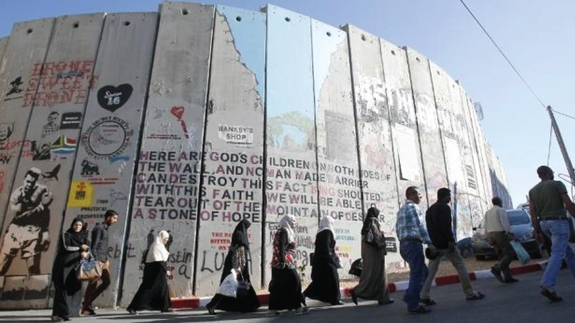 فلسطينيون يمرون بجانب جدار الفصل الإسرائيلي في صورة من الأرشيف 