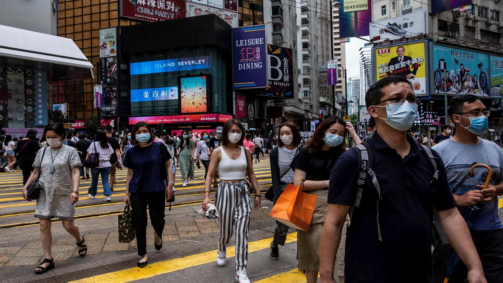 الناس يعبرون طريقًا في منطقة التسوق المزدحمة في خليج كوزواي في هونغ كونغ