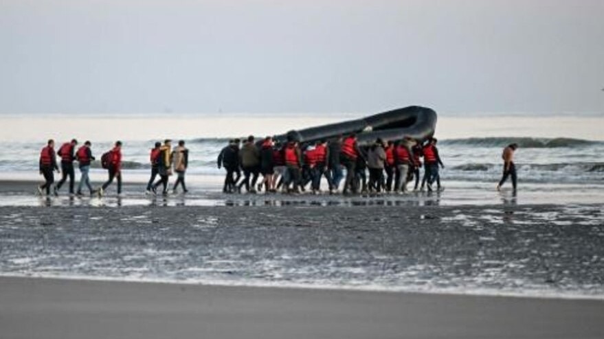 عشرات المهاجرين يحملون زورقا مطاطيا قبيل محاولتهم عبور المانش، قرب مدينة غرافلين بشمال فرنسا في 11 يوليو 2022