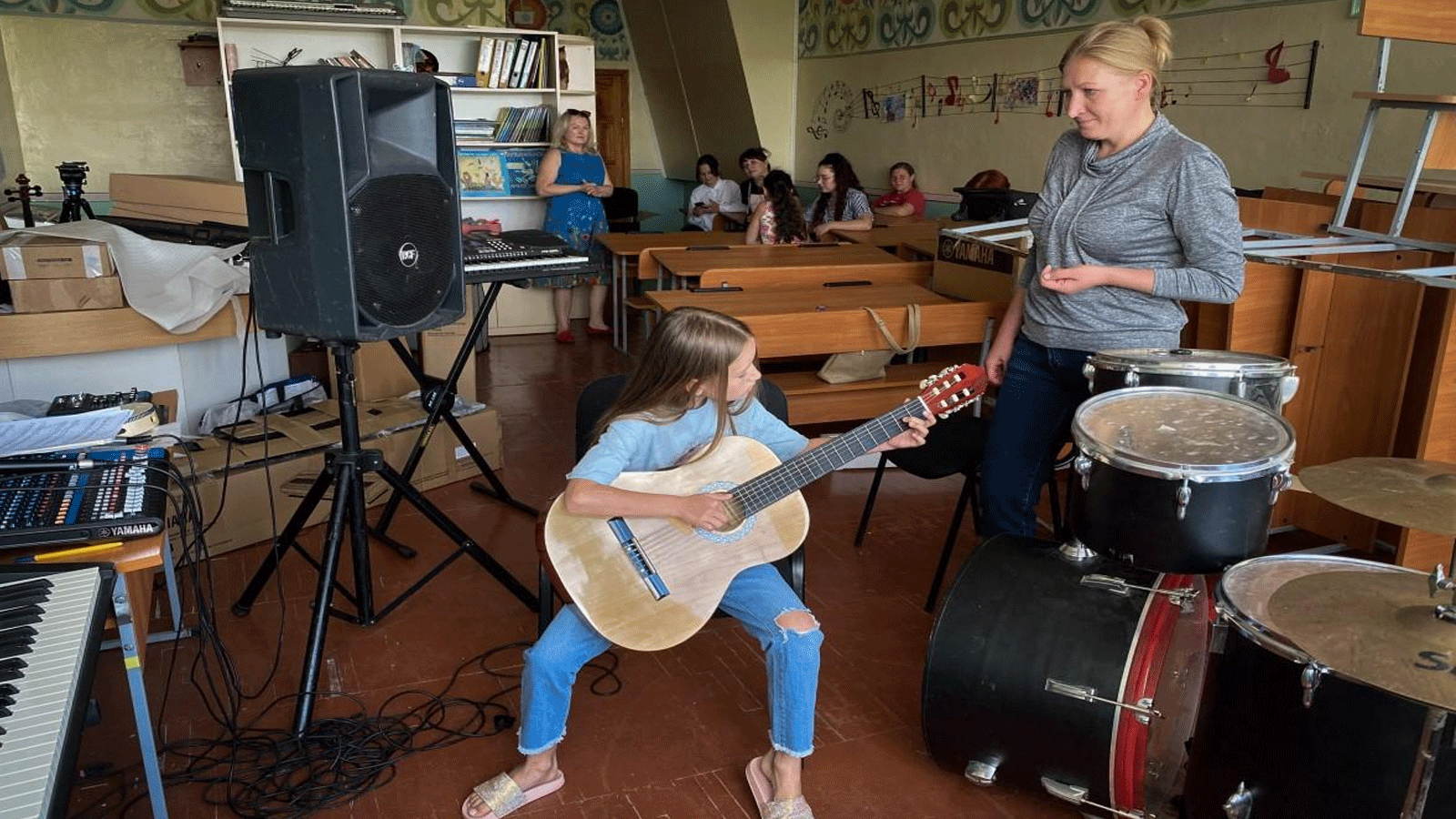 فتاة تعزف على الغيتار بتعليمات من معلمتها تيتيانا كريفوشينكو في بوروديانكا
