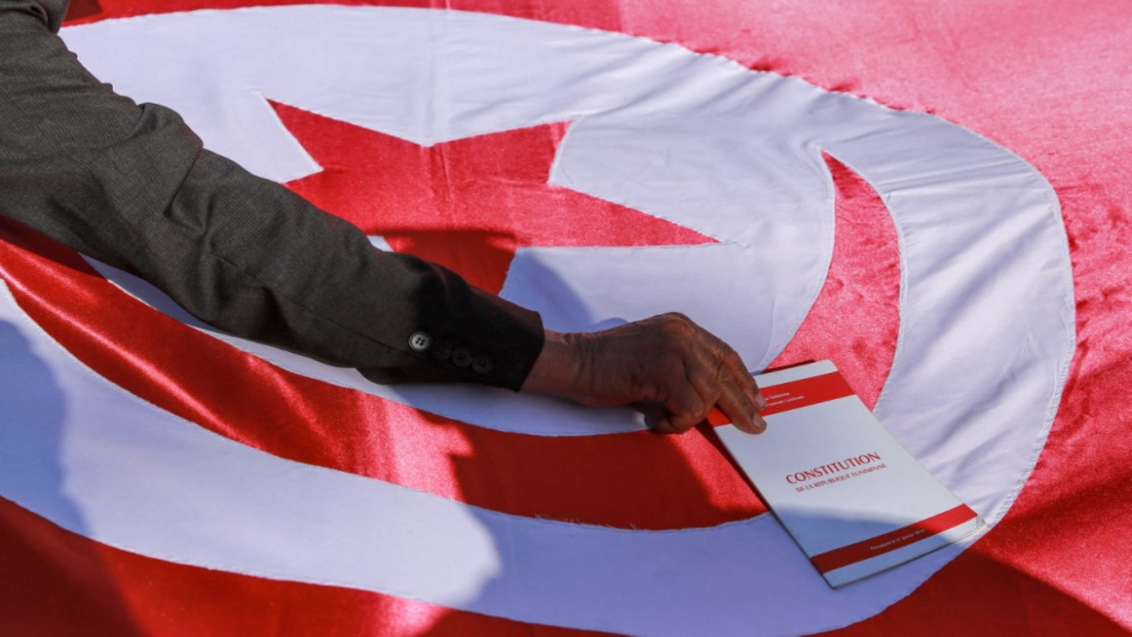 رجل يحمل نسخة من الدستور التونسي على علم بلاده خلال تظاهرات ضد قرارات الرئيس قيس سعيد