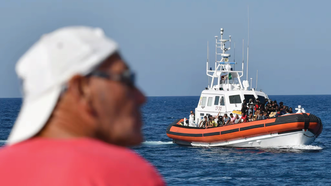 رجل يراقب مهاجرين من تونس وليبيا يصلون إلى ساحل إيطاليا