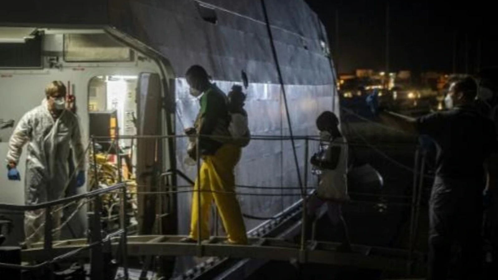 مهاجرون يستقلون سفينة غوراديا دي فينانزا وسفينة عسكرية تابعة للبحرية قبل نقلهم من منشأة معالجة تشغيلية للمهاجرين في جزيرة لامبيدوزا جنوب إيطاليا جنوب صقلية إلى مركز آخر في 10 يوليو 2022