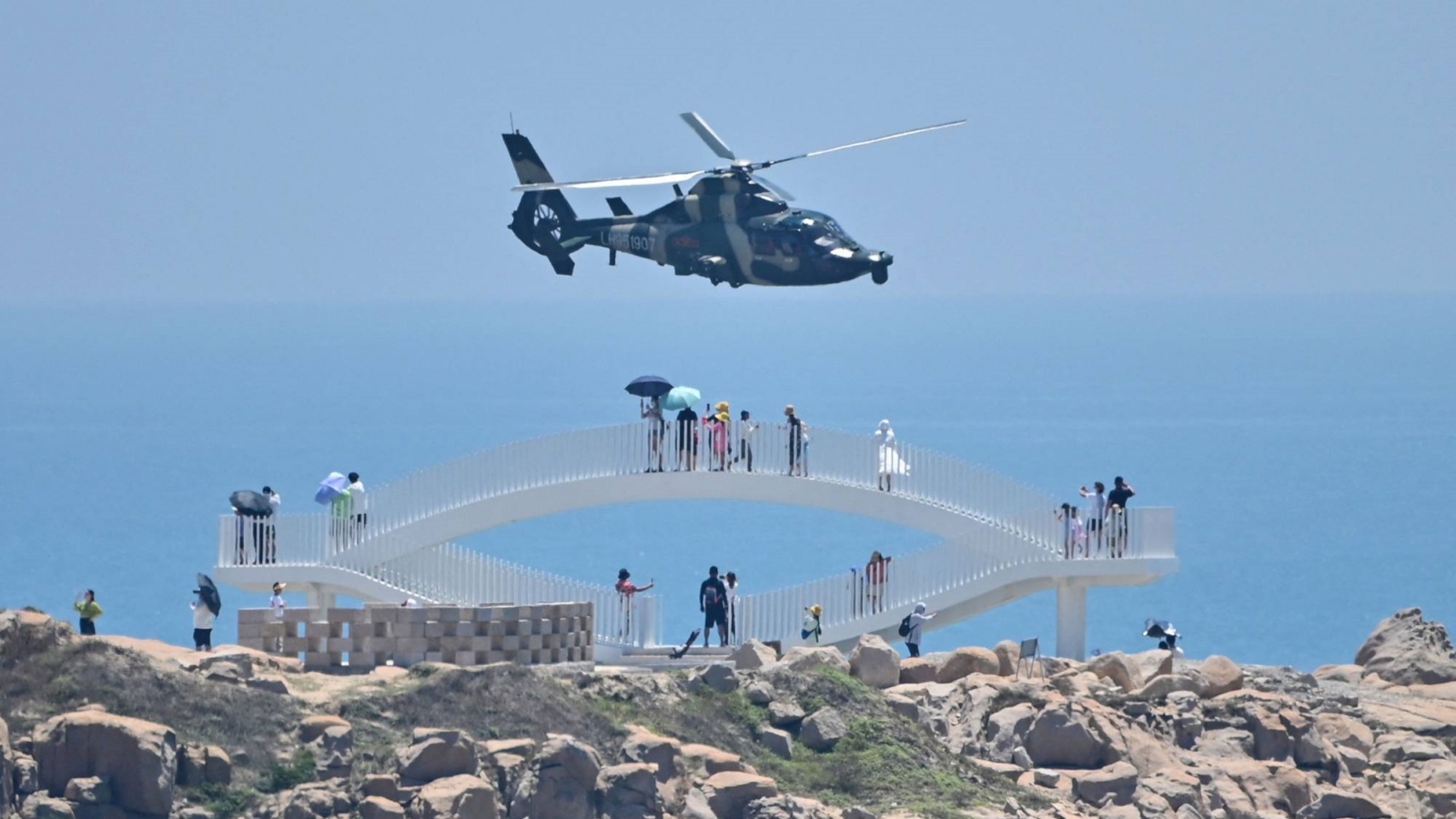 سائحون ينظرون إلى طائرة هليكوبتر عسكرية صينية تحلق فوق جزيرة بينغتان ، إحدى أقرب نقاط البر الرئيسي للصين لتايوان ، في مقاطعة فوجيان يوم الخميس 4 أغسطس 2022، قبل مناورات عسكرية ضخمة قبالة تايوان
