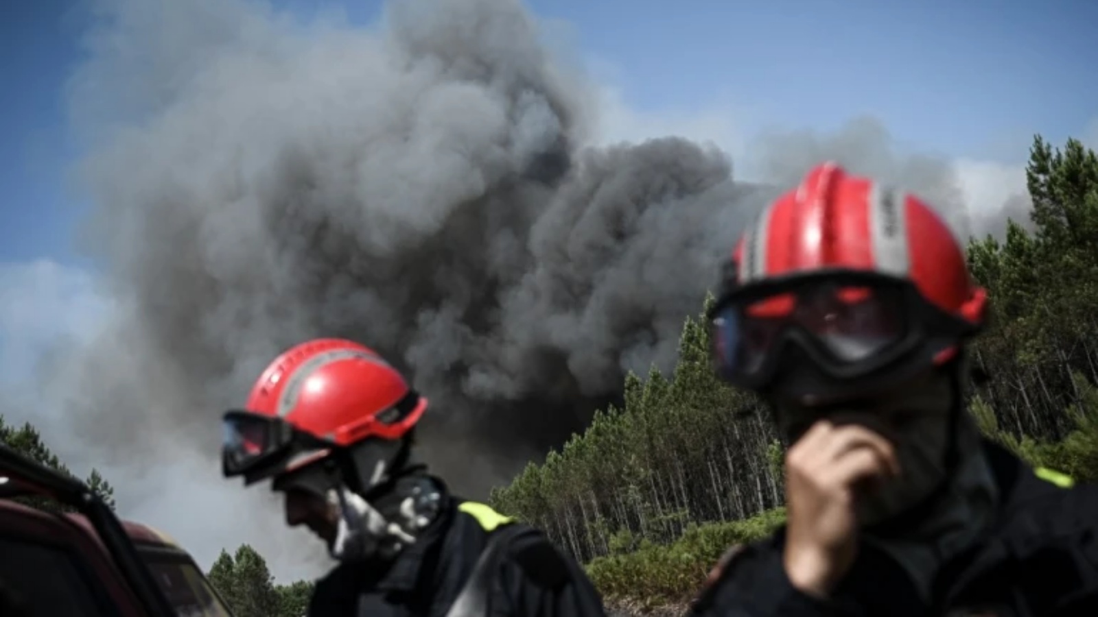 رجال الإطفاء على طريق حيث شوهد دخان كثيف في الخلفية أثناء حرائق الغابات بالقرب من مدينة أورين، فرنسا