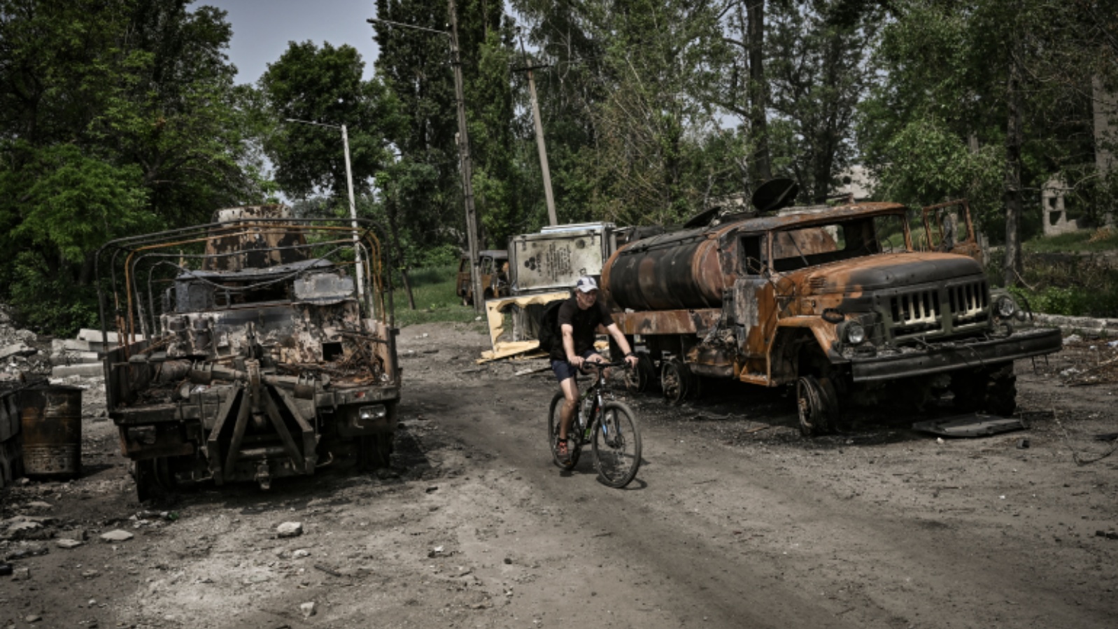 رجل يركب دراجته بين شاحنتين عسكريتين مدمرتين في مدينة ليسيتشانسك، منطقة دونباس بشرق أوكرانيا، في 11 يونيو 2022