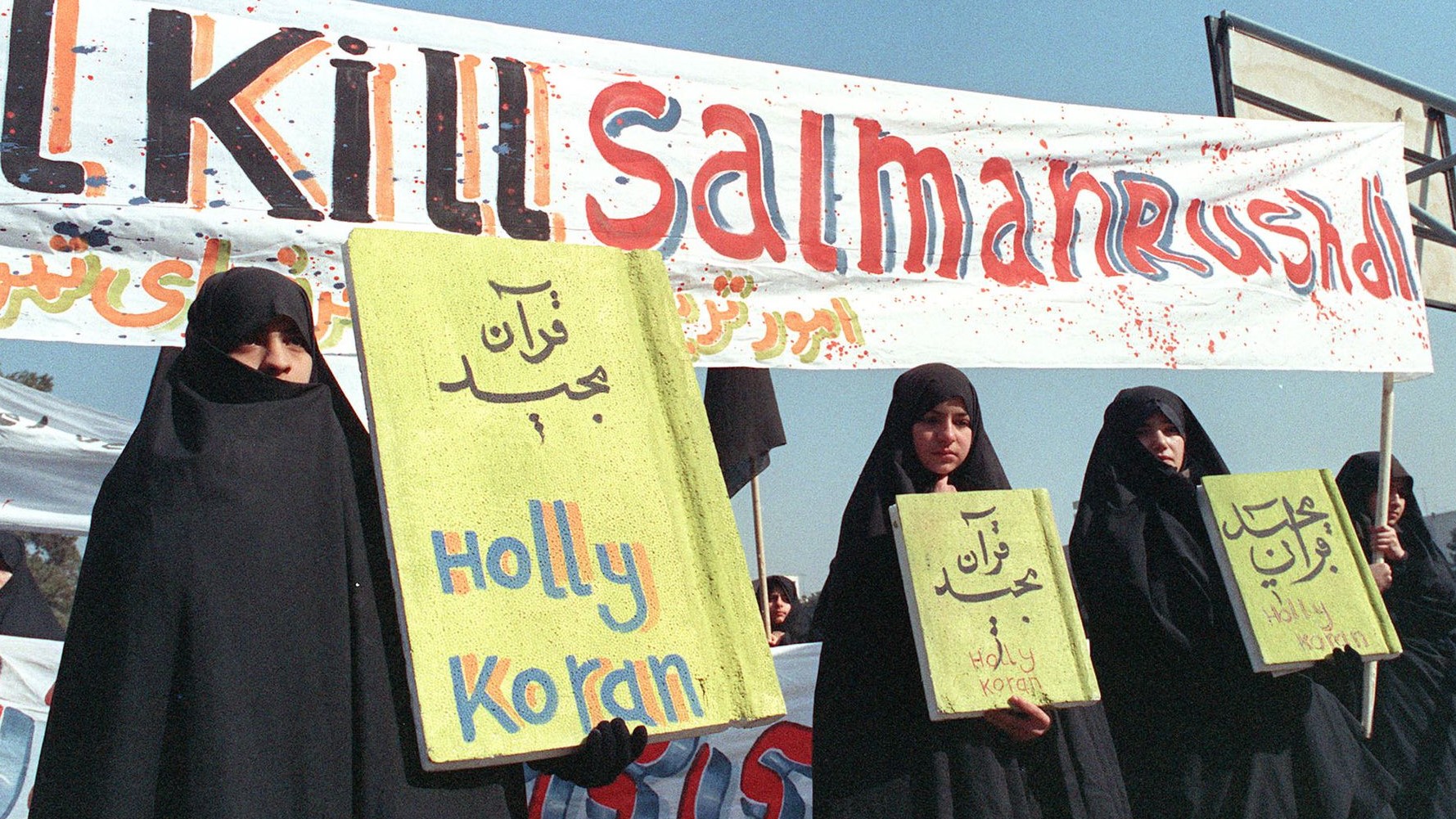 في هذه الصورة الأرشيفية التي التقطت في 17 فبراير/شباط 1989، تظهر نساء إيرانيات يحملن لافتات كتب عليها 'هولي كوران' و'اقتلوا سلمان رشدي' خلال مظاهرة ضد الكاتب البريطاني سلمان رشدي في طهران.